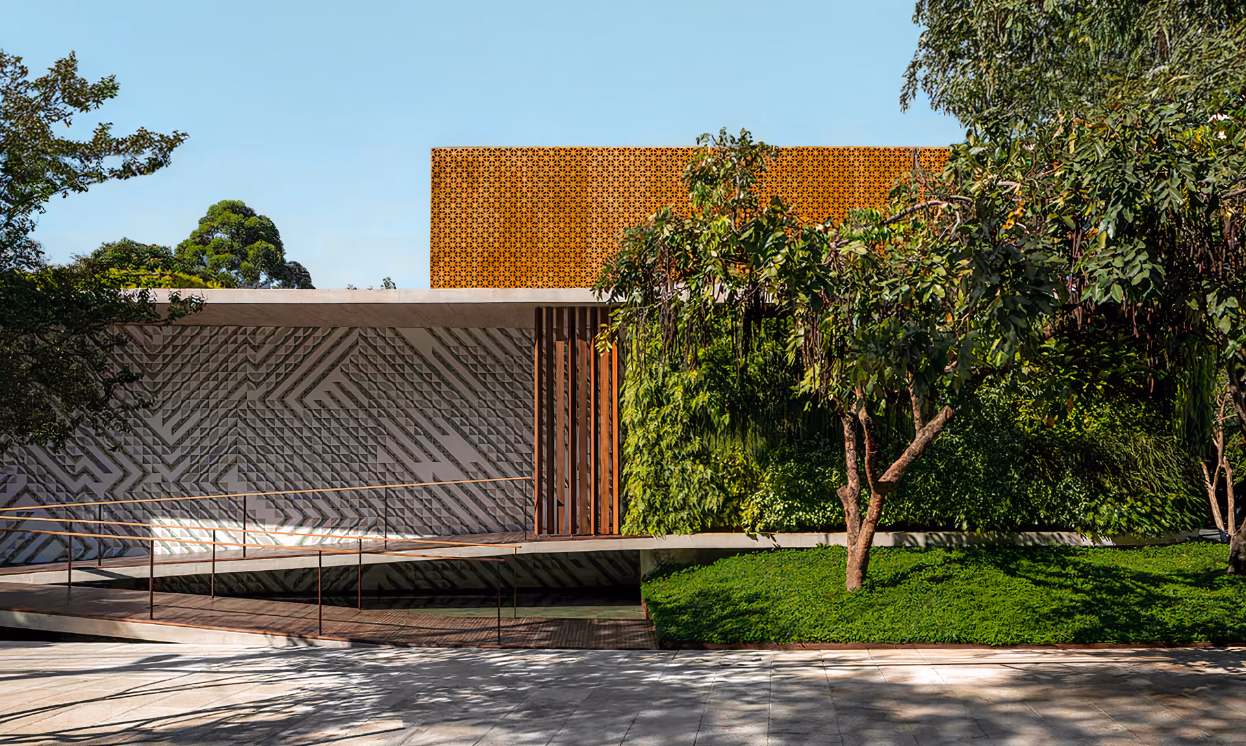 Aigai Spa exterior with a patterned concrete wall, planted facade and entrance ramp shaded by trees.