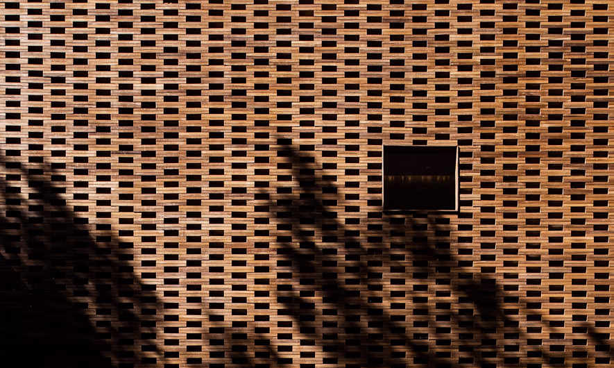 Perforated brick facade at Beldi Lab, with a square window and shadows cast by nearby trees.