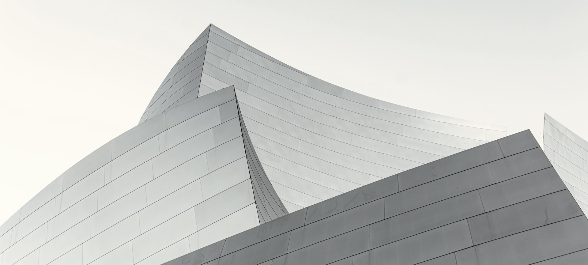 Overlapping curved metal walls of a modern building, photographed in black and white.
